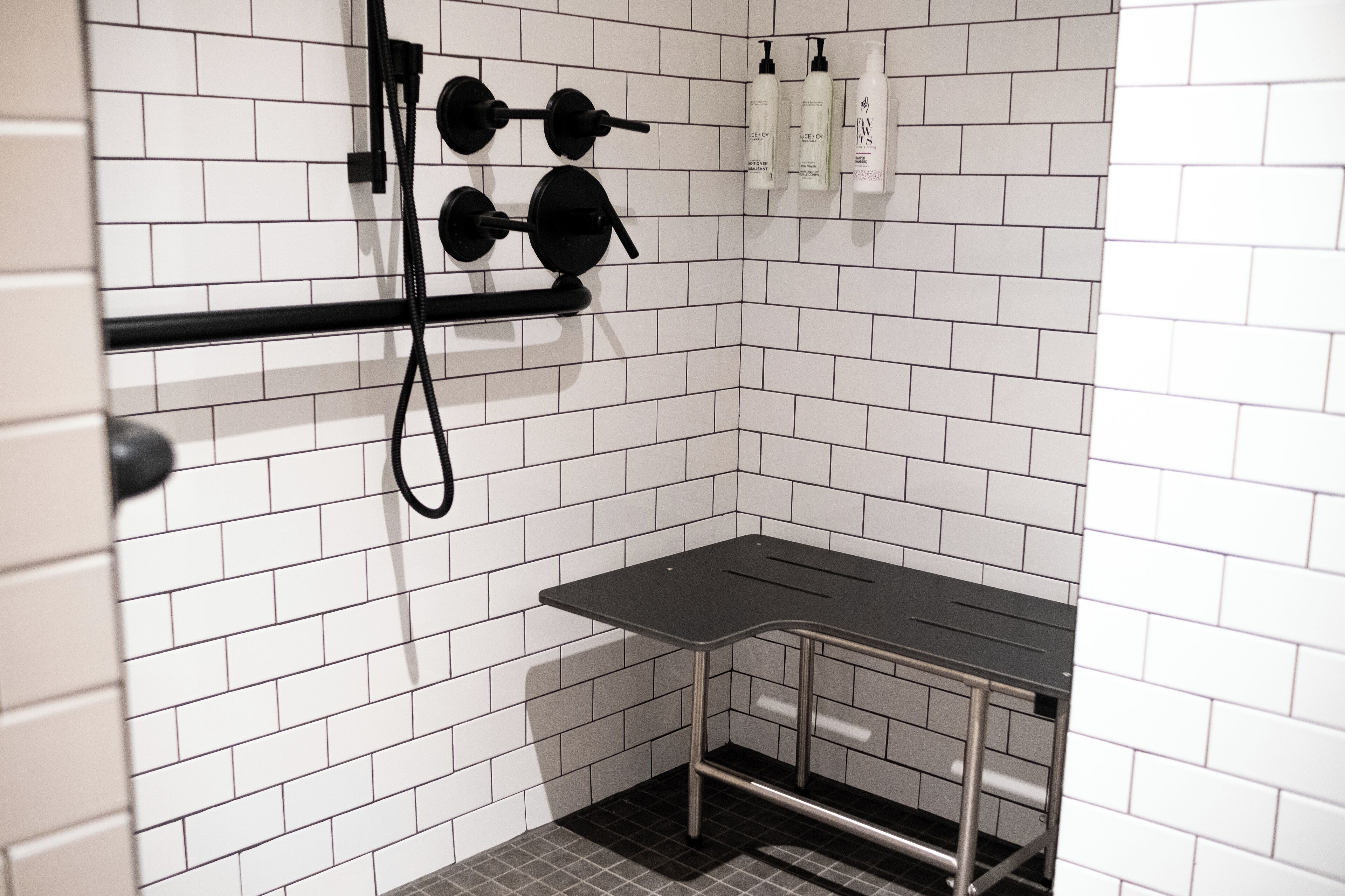 A bathroom with white tiled walls, a black towel rack, and a small table.