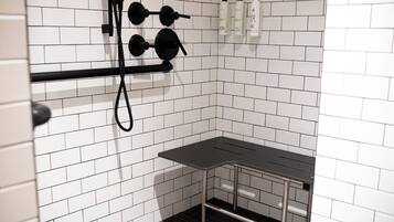 A bathroom with white tiled walls, a black towel rack, and a small table.
