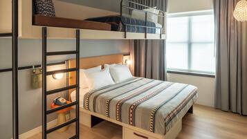 A bunk bed room with a ladder, a bedside table, a lamp, and a window with curtains.