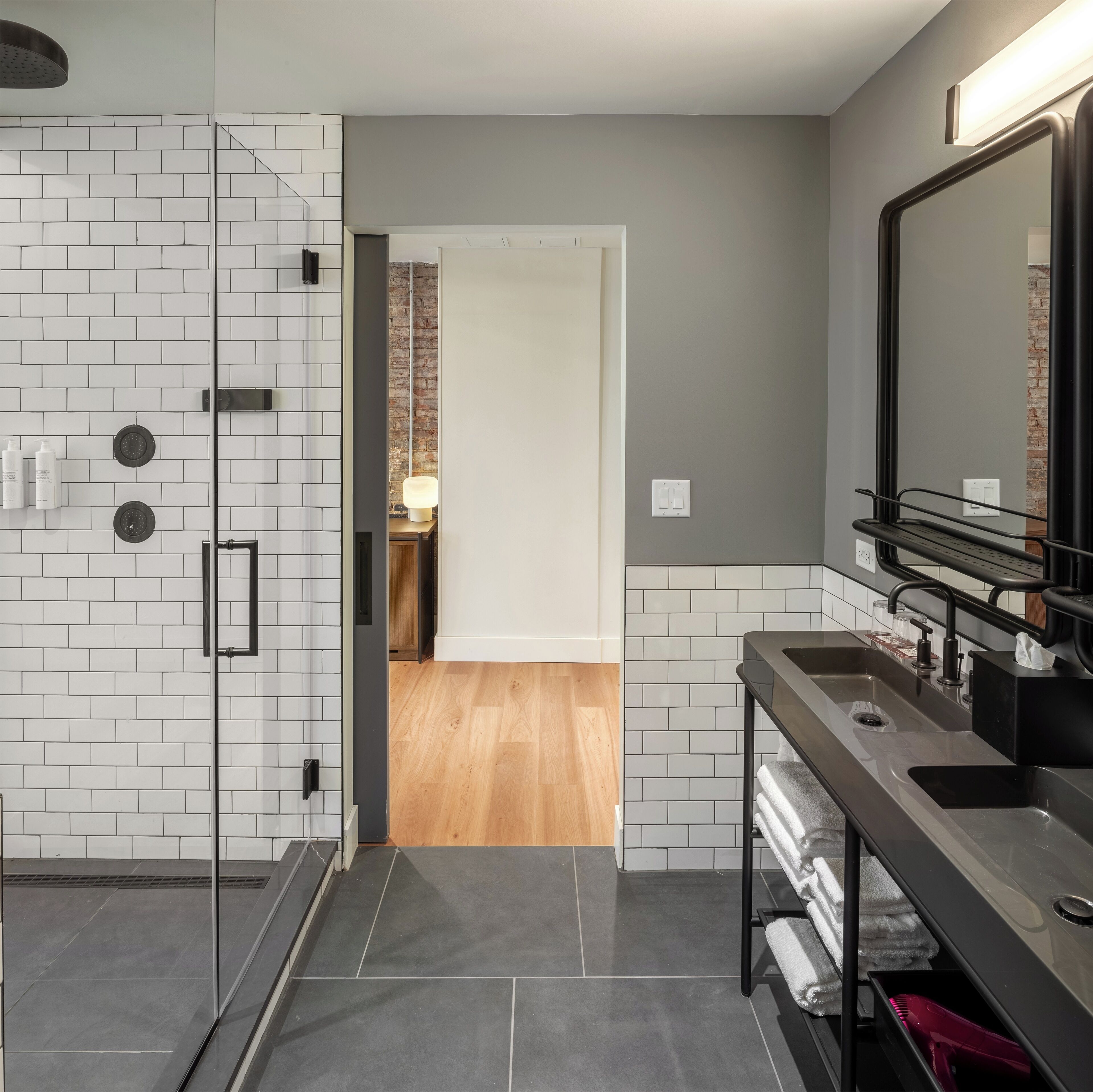 A modern bathroom with a glass shower enclosure, a black sink with a mirror, and a wooden floor.