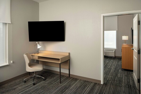 Habitación de hotel con escritorio, silla, televisión de pantalla plana, lámpara y vista al pasillo.