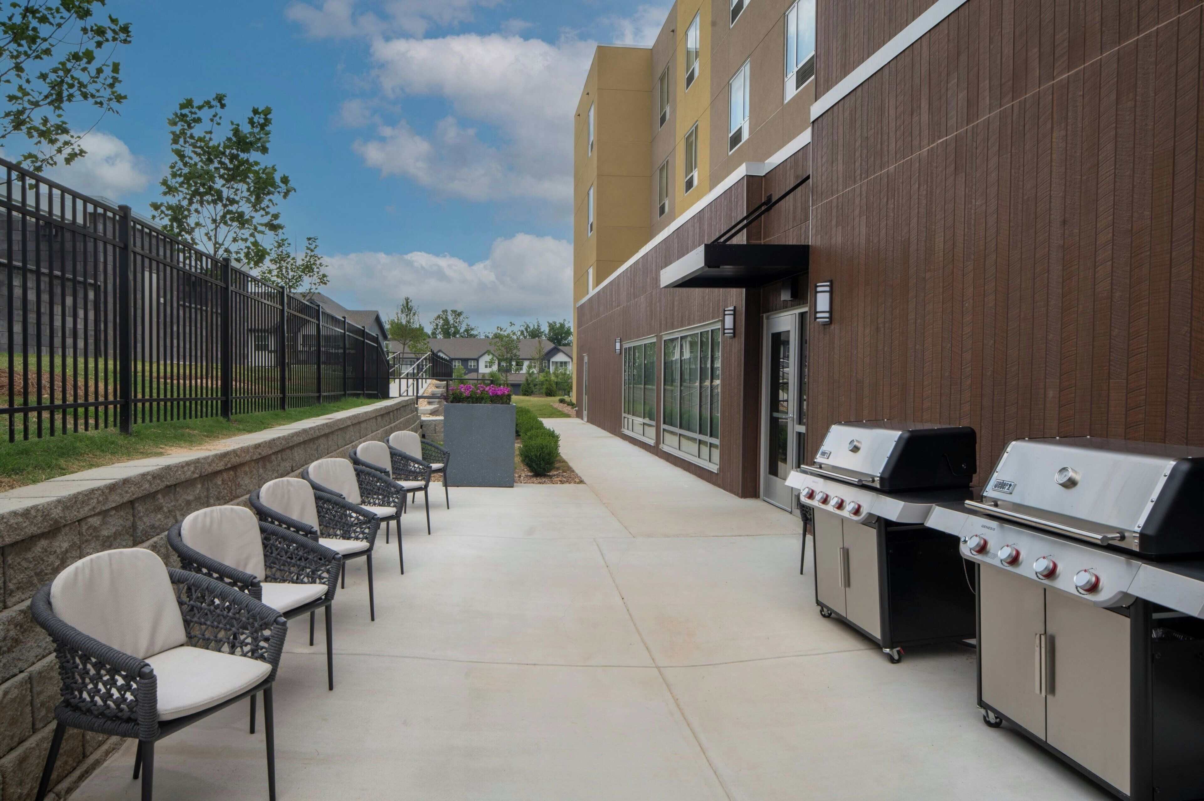 An outdoor patio with a barbecue grill, wicker chairs, and a stone wall.