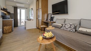 A modern living room with a sofa, a dining table with fruit, a TV, and a kitchen area. - Almi of Naxos (Naxos)