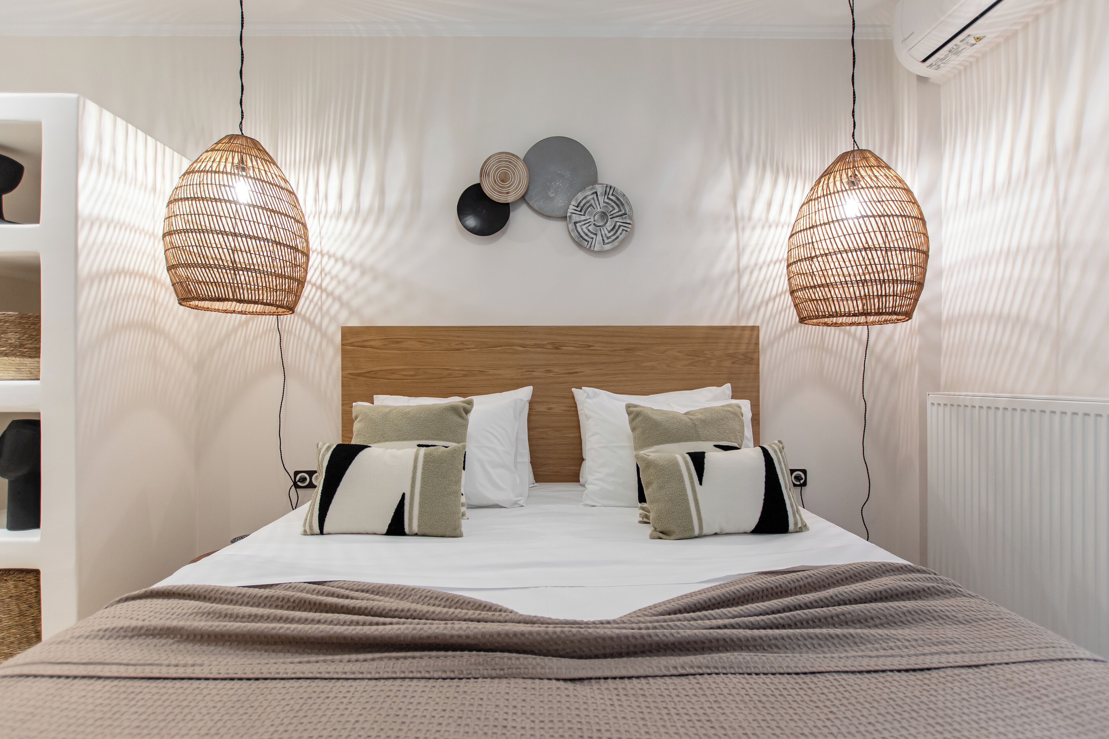 Una cama bien hecha con un cabecero de madera, dos lámparas de mimbre colgantes y una pared decorada con platos.