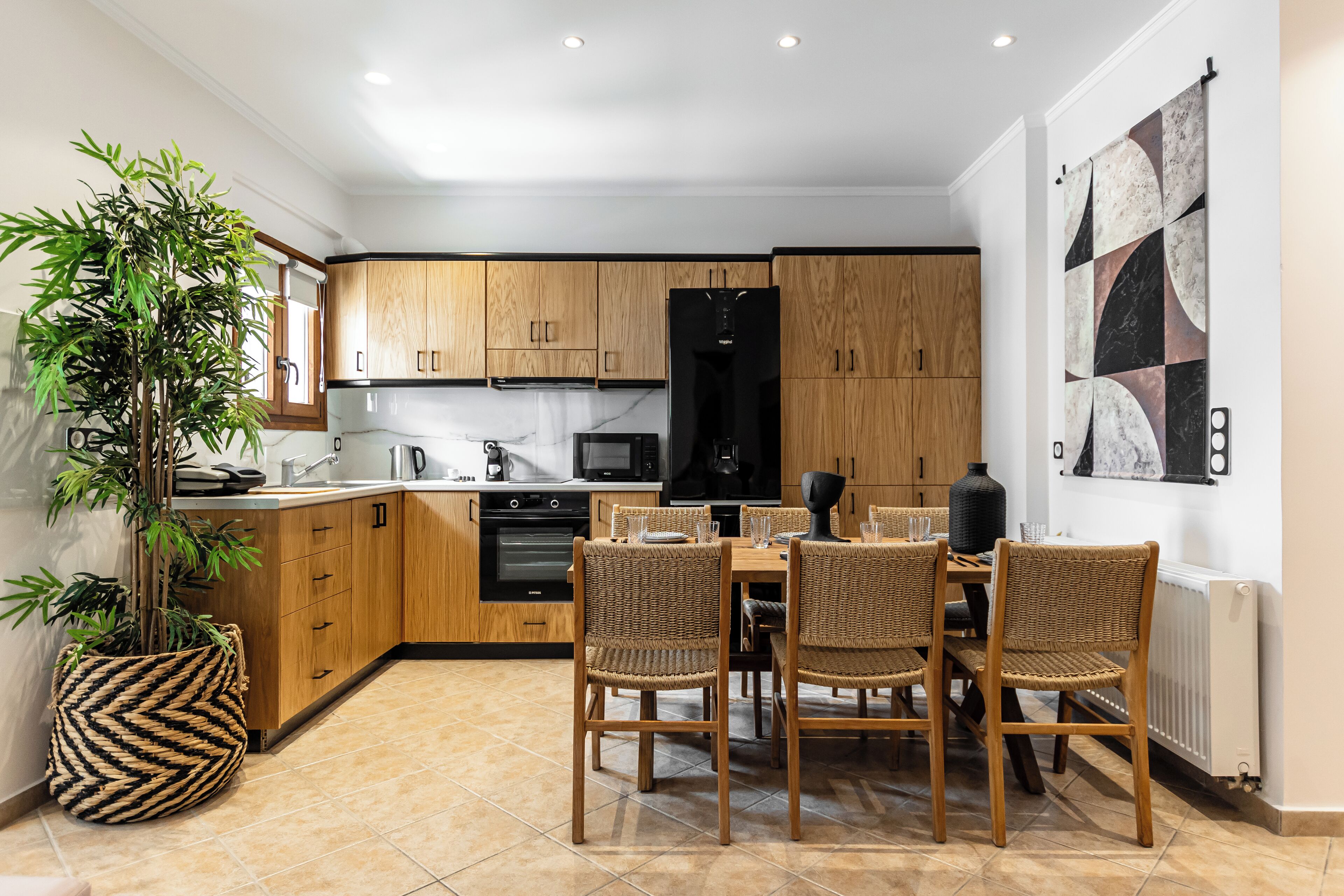 Une cuisine moderne avec des meubles en bois, une table à manger avec des chaises, une grande plante en pot et un pare-feu en marbre.