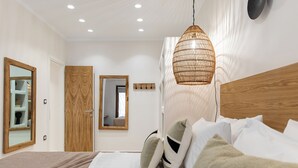 A modern bedroom with a wooden headboard, a large mirror, and a hanging light fixture. - Almi of Naxos (Naxos)