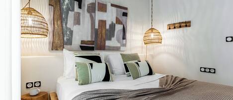 A neatly made bed with a patterned blanket, two bedside lamps, a wall-mounted artwork, and a small bedside table with a cup.
