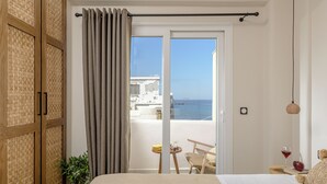 A bedroom with a bed, a small table with a plant, a chair, and a view of the sea through a sliding door. - Almi of Naxos (Naxos)