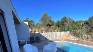 A poolside area with white plastic chairs and a table, surrounded by a wooden deck.