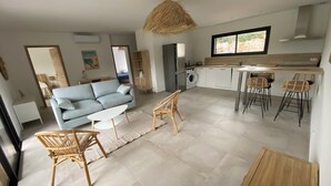 A modern living room with a sofa, chairs, a coffee table, and a kitchen area with a dining table and chairs.