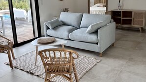 A modern living room with a light blue sofa, a wicker chair, a woven coffee table, and a large mirror.