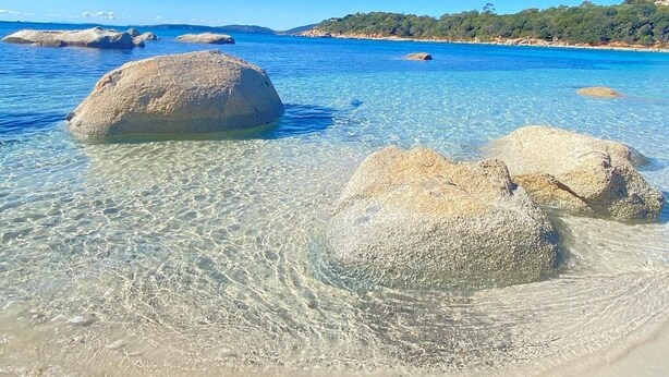 A clear blue sea with large rocks in shallow water.