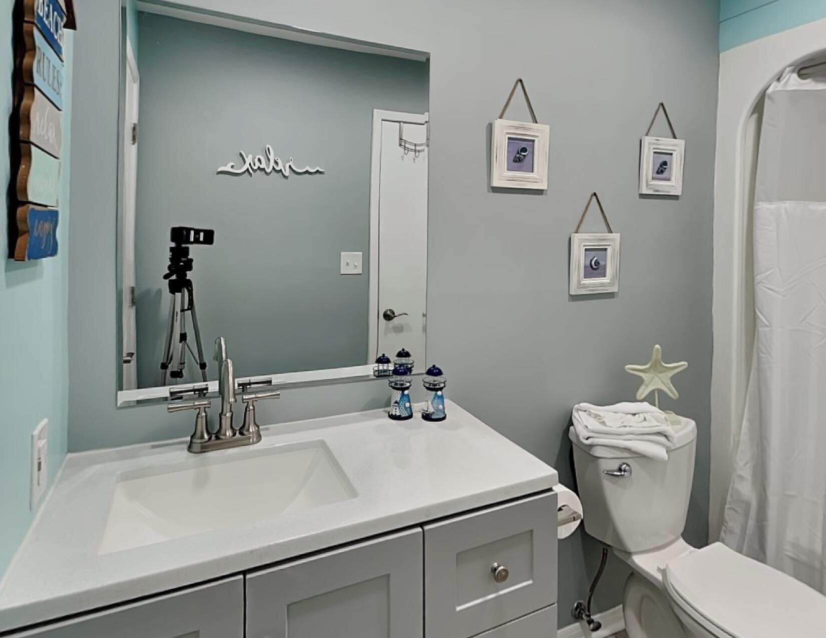 A bathroom with a white sink, mirror, and toilet. There are decorative items like a starfish and framed pictures on the wall.