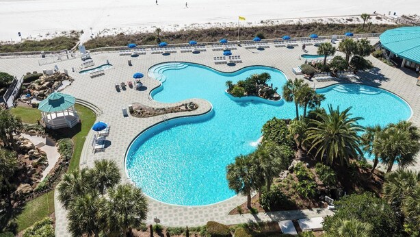 A resort with a large, winding pool surrounded by palm trees and lounge chairs. - Turtle Cay Golf Villa Edgewater Beach Resort (Panama City Beach)