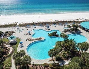 Um resort com uma piscina grande e sinuosa, cercada por palmeiras e espreguiçadeiras.