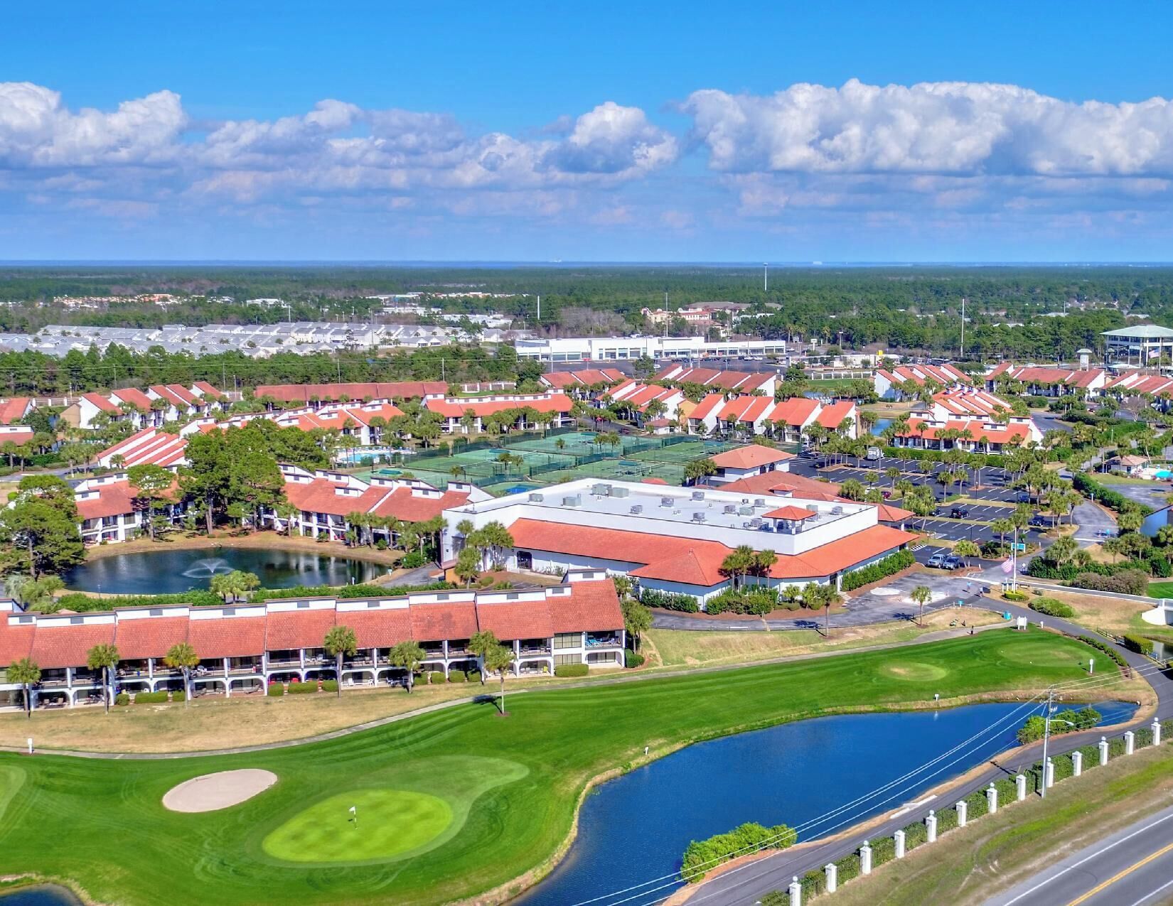 Un campo de golf con club house, canchas de tenis y una amplia zona de estacionamiento.