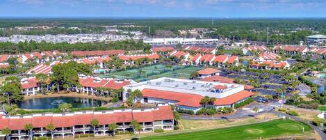 Un campo de golf con club house, canchas de tenis y una amplia zona de estacionamiento.