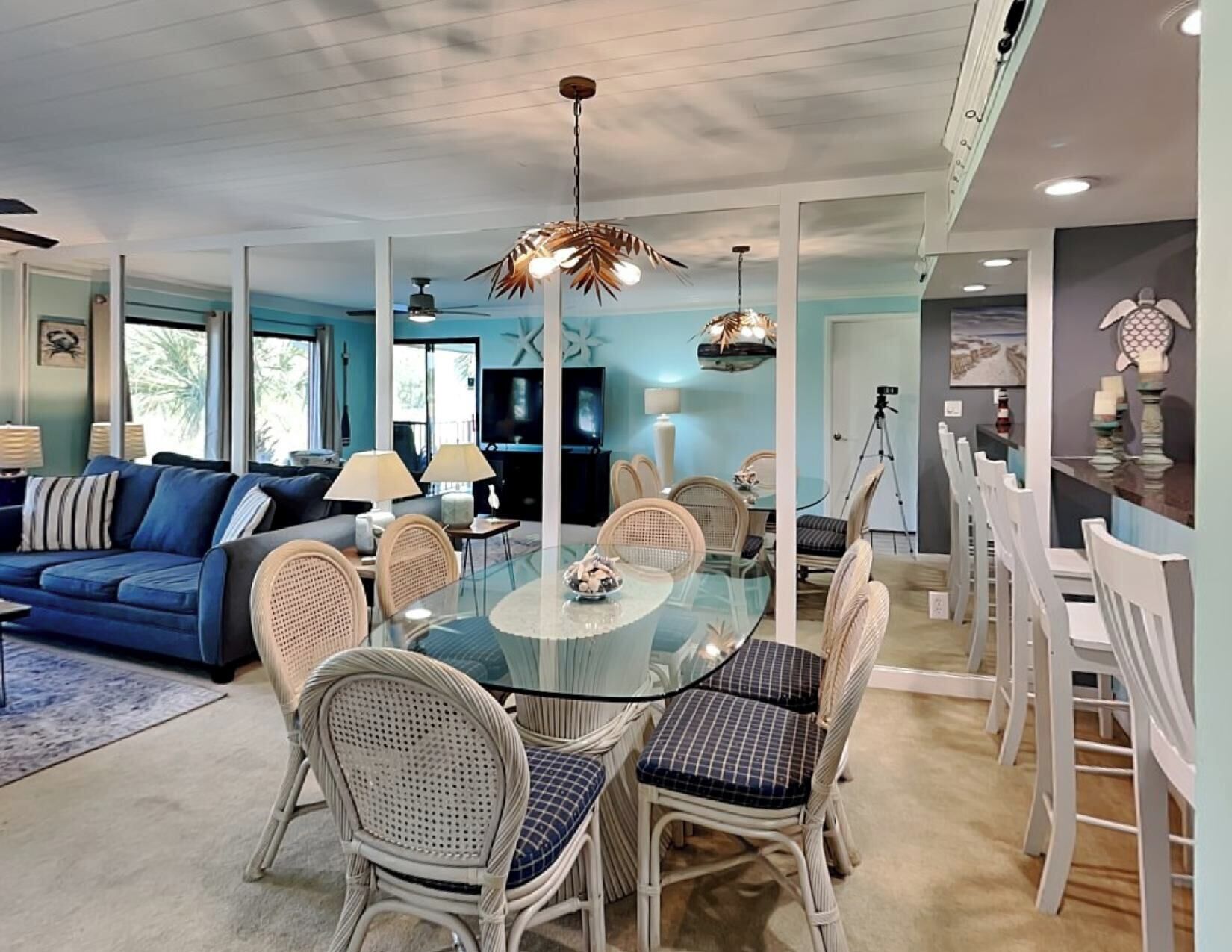 A spacious living room with a blue sofa, a glass dining table surrounded by wicker chairs, and a ceiling fan.