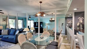A spacious living room with a blue sofa, a glass dining table surrounded by wicker chairs, and a ceiling fan. - Turtle Cay Golf Villa Edgewater Beach Resort (Panama City Beach)