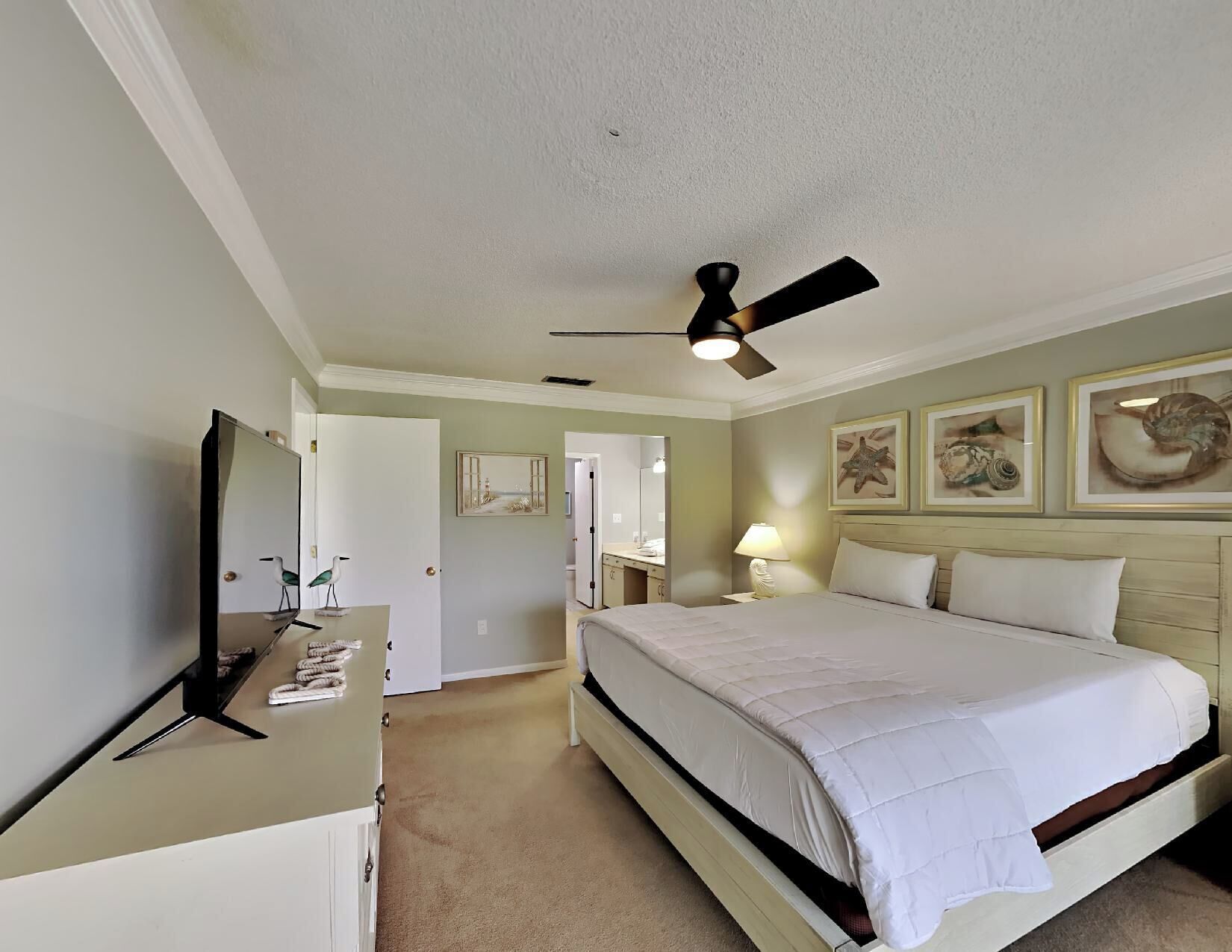 A hotel room with a bed, a desk, a ceiling fan, and artwork on the walls.