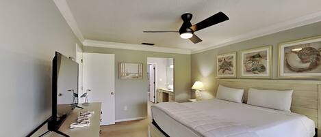 A hotel room with a bed, a desk, a ceiling fan, and artwork on the walls.