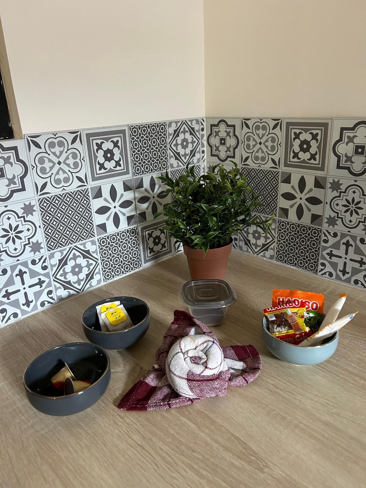 Uma cozinha com ladrilhos estampados, uma planta em vaso e diversos utensílios de cozinha, incluindo tigelas e um pano.