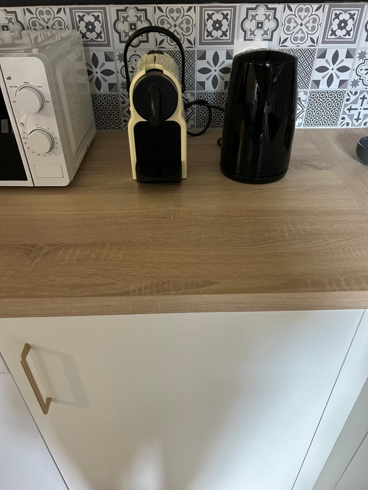 A kitchen with a microwave, a black coffee maker, and a white cabinet.