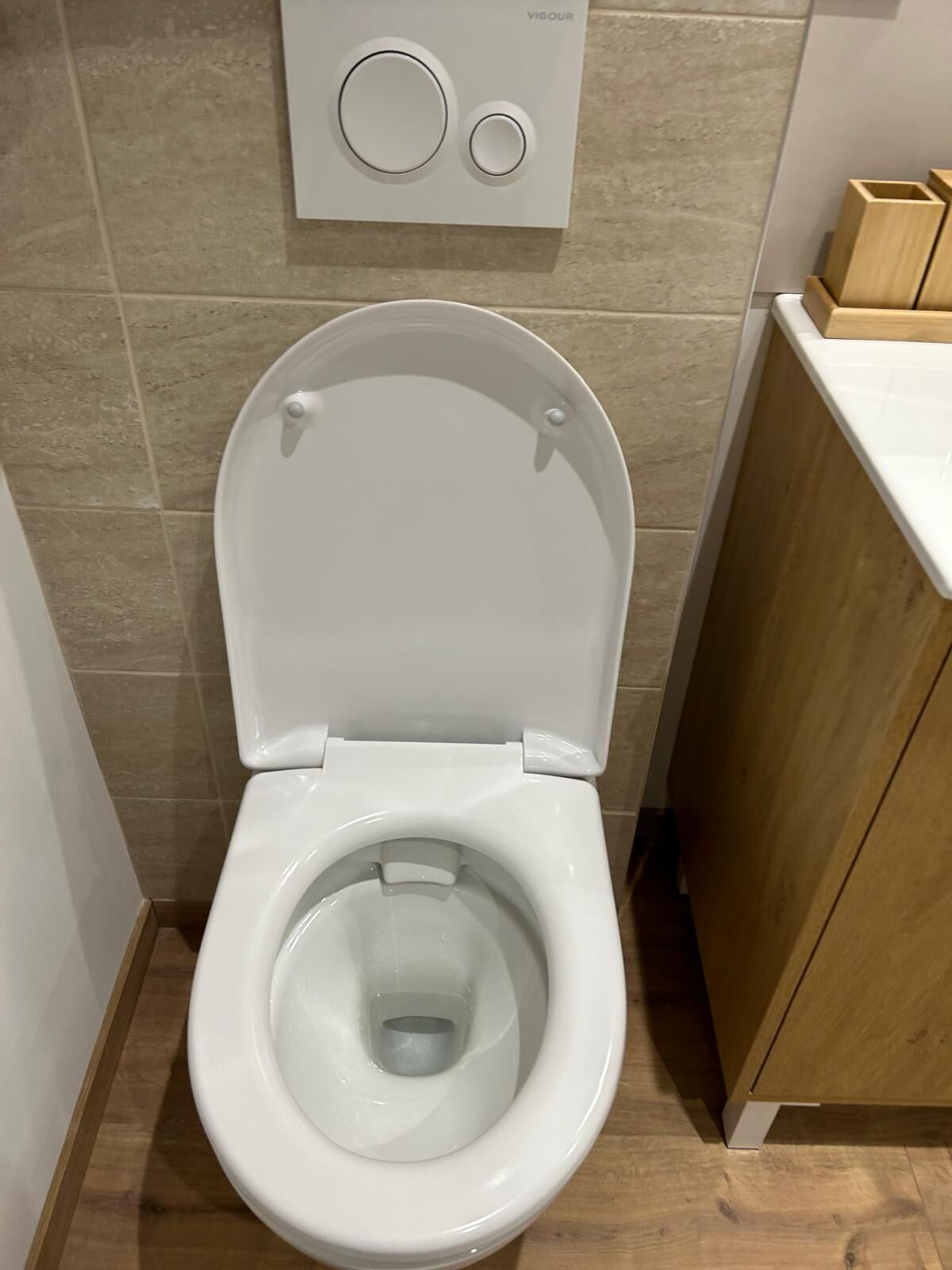 Un moderno water con il coperchio abbassato, pulsante a muro e un armadietto in legno alla destra.