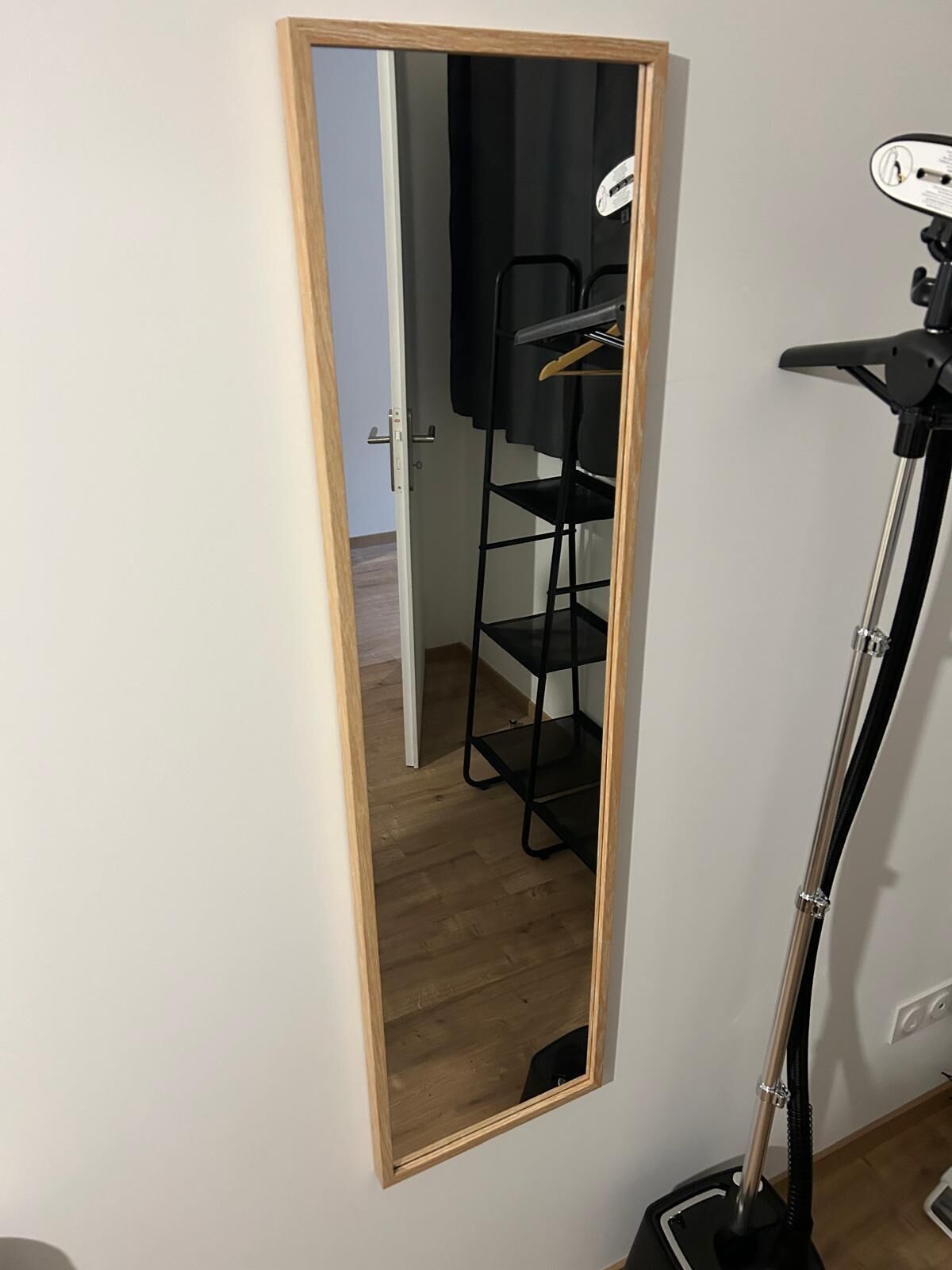 Een spiegel met houten lijst, een zwarte vloerlamp en een zwarte stoel met kapstok.