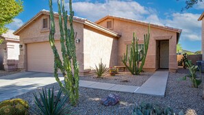 Une maison avec un garage, entourée de cactus et de plantes du désert.