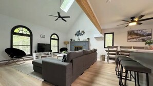 Ein geräumiges Wohnzimmer mit grauem Sofa, einem schwarzen Sessel, Holzboden und Kamin.