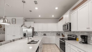 A modern kitchen with white cabinetry, a large island with a sink, stainless steel appliances, and pendant lighting.
