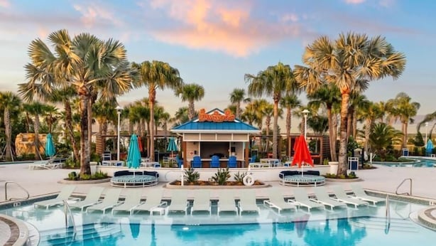 A pool area with lounge chairs, a bar, and palm trees.