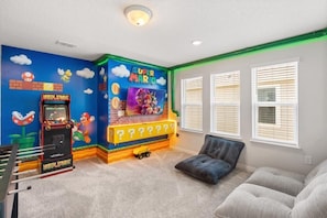 Quarto com parede decorada com tema Mario, um sofá e uma janela com persianas.