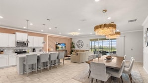 A modern kitchen with a central island, bar stools, and a dining area with a large wooden table and chairs.