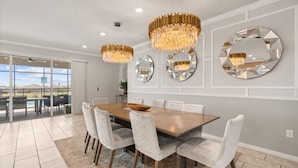 A dining area with a large table, white chairs, and three chandeliers.