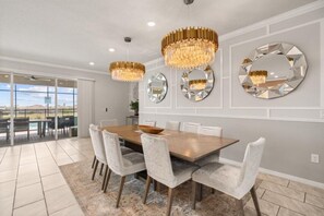 A dining area with a large table, white chairs, and three chandeliers.