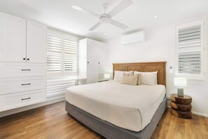 A bedroom with a bed, white cabinets, a ceiling fan, and a bedside table with a lamp.