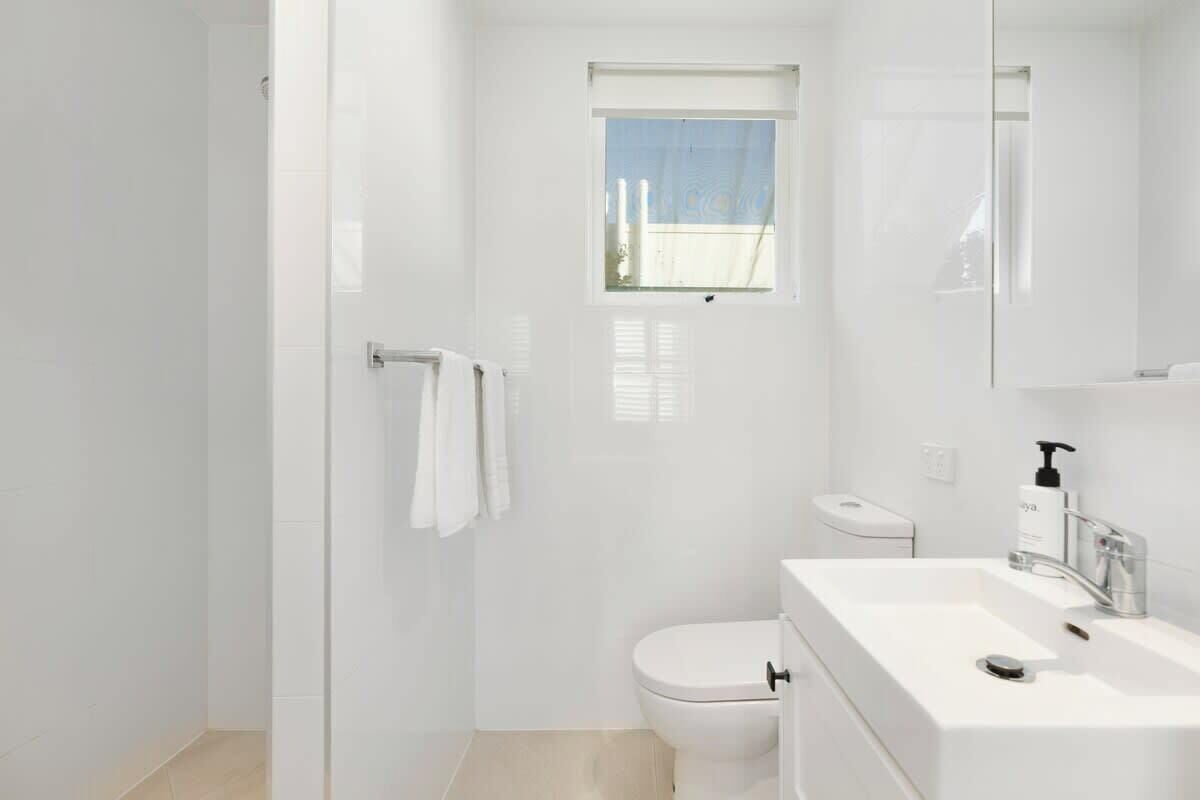 A modern bathroom with a white sink, toilet, and glass shower enclosure.