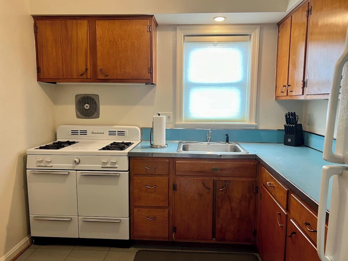 Une cuisine de taille réduite, avec des meubles de rangement en bois, une cuisinière, un évier et une fenêtre.