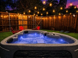 A hot tub with a wooden fence and string lights in the background.