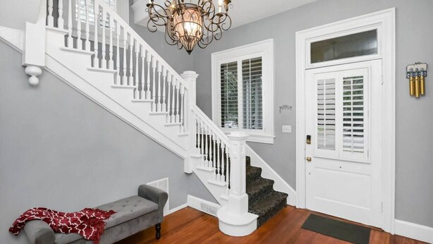 Un escalier avec des balustrades blanches, un lustre et un banc recouvert d’un plaid rouge.