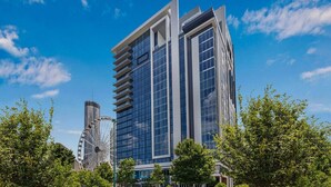 Un moderno edificio de gran altura con amplios ventanales y una noria al fondo.