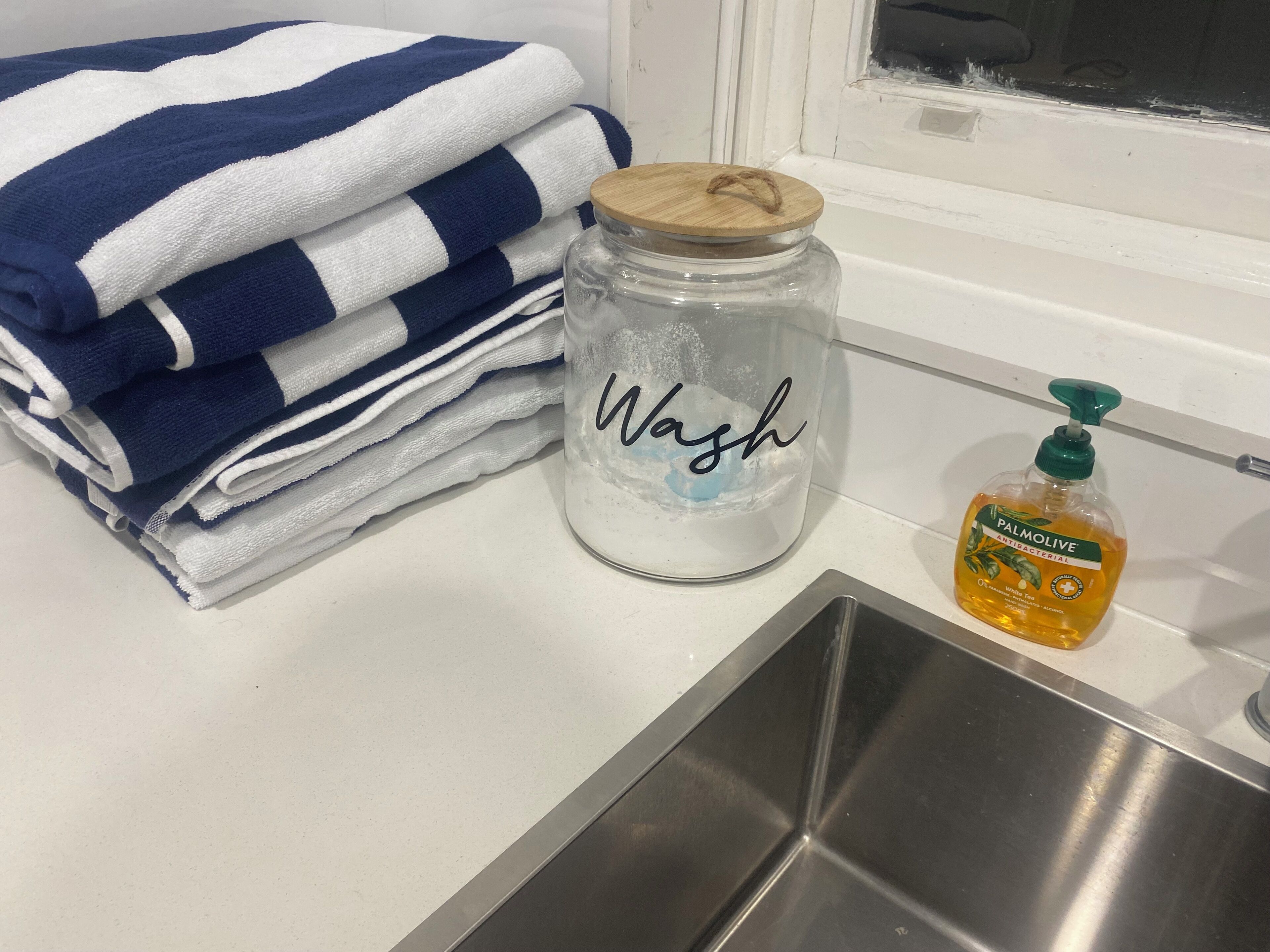 Ein Küchenspülbecken, ein mit ‚Waschen‘ beschriftetes Glas und eine Flasche antibakterieller Palmolive Seife.