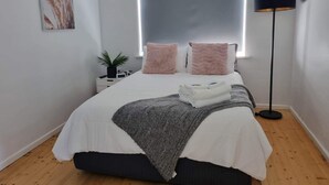 A modern bedroom with a bed, bedside table, lamp, and a wall-mounted artwork. - LUXURY HOME  WITH KING BED, HOT TUB, WiFi, AC , Arcade games Netflix sleeps 9  (Portland)