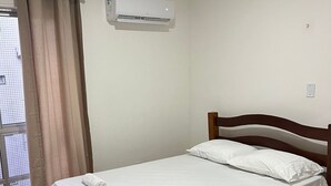 A single bed with a wooden headboard, white bedding, and a rolled towel on the footboard. An air conditioning unit is mounted on the wall above the bed. - Spacious 3-bedroom apartment in amazing Boa Viagem Recife with AC, WiFi (Boa Viagem Recife)