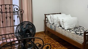 A bedroom with a wooden bed, a metal-framed chair, a standing fan, and a window with curtains. - Spacious 3-bedroom apartment in amazing Boa Viagem Recife with AC, WiFi (Boa Viagem Recife)