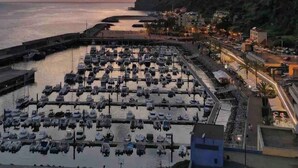 Un puerto deportivo con numerosas embarcaciones amarradas, una carretera costera y edificios a lo largo del acantilado.