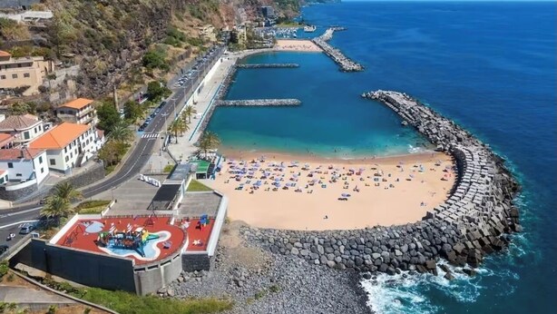 Una playa costera con un rompeolas rocoso, un parque infantil y una carretera que lleva a la playa.