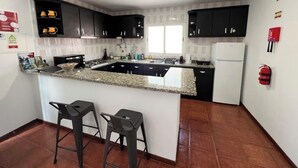 Una cocina con gabinetes negros, encimera de granito, una isla integrada con taburetes de bar y un refrigerador.